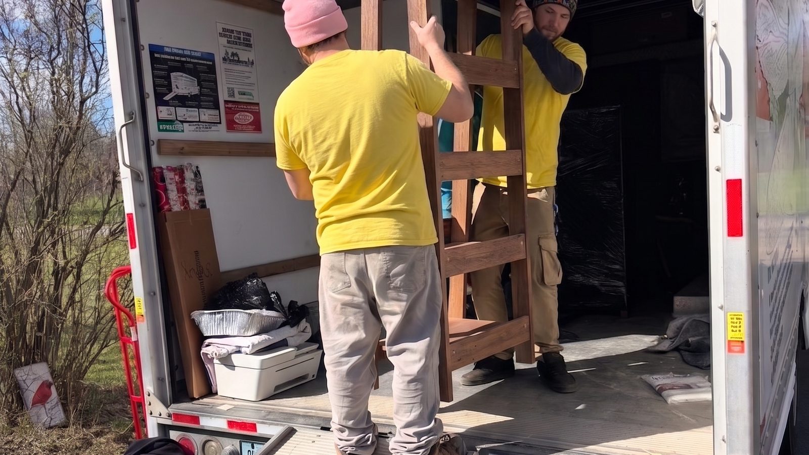 A Hercules mover in a yellow shirt loading a wrapped bunk bed frame into the back of a moving truck