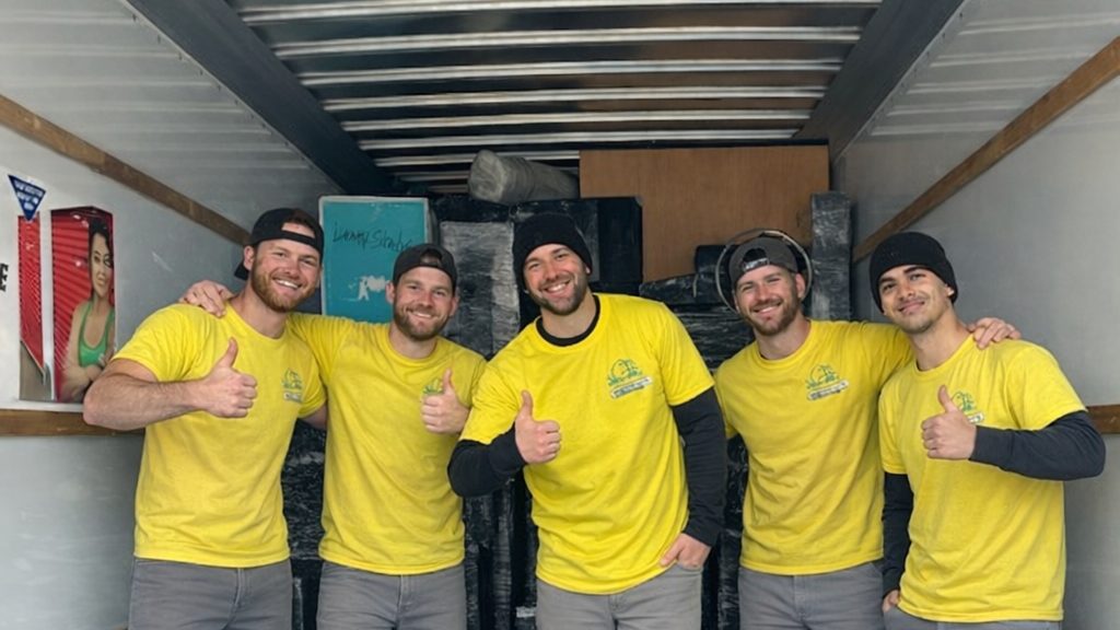 Five Hercules movers in matching yellow shirts giving a thumbs up inside an empty moving truck