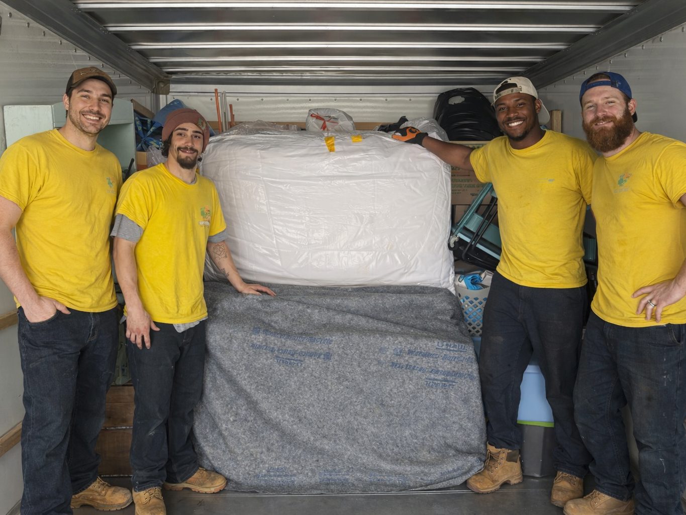 Four Hercules movers holding a wrapped mattress inside a truck