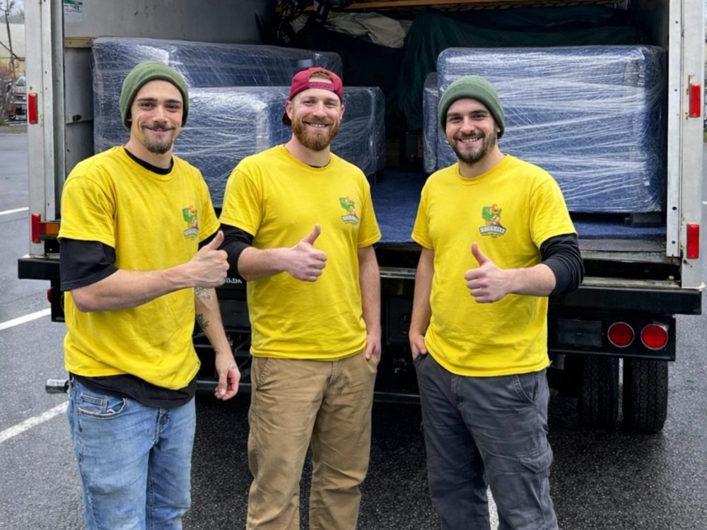 Three Hercules movers giving a thumbs up in front of a box truck loaded with furniture wrapped in blue moving blankets