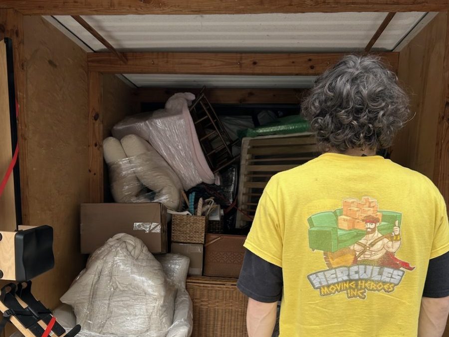 A Hercules mover, back to the camera, at the open door of a truck packed tight with boxes and wrapped furniture