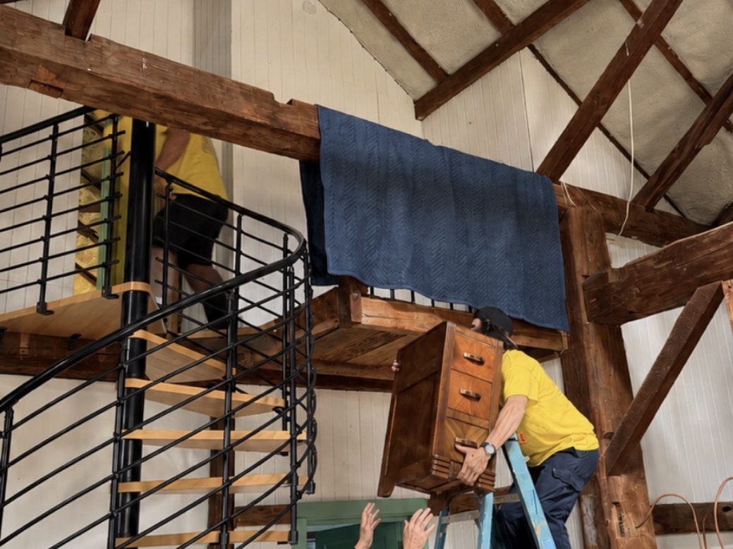 A Hercules mover carrying a wrapped cabinet down a spiral staircase in a barn