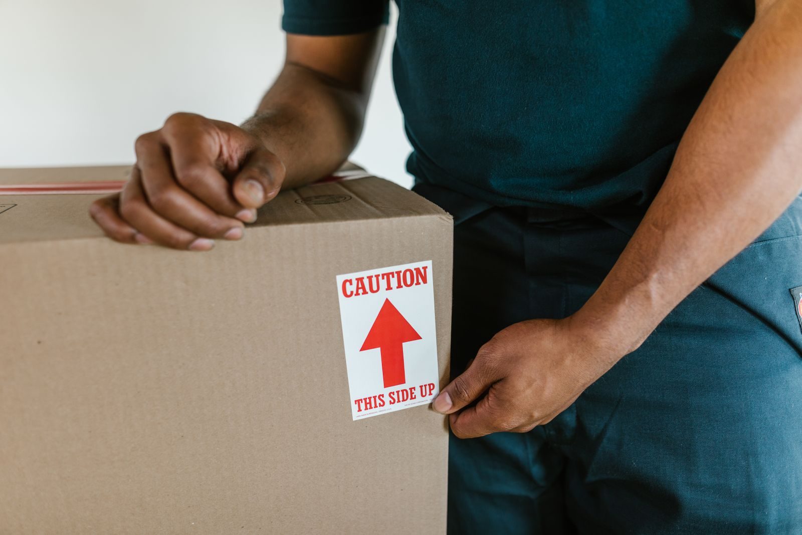 A mover's hands holding a cardboard box with a caution this side up label