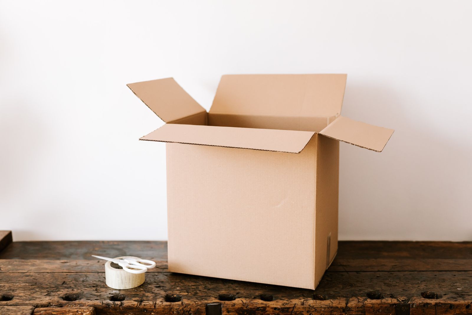 An open cardboard box and a roll of tape on a wooden table