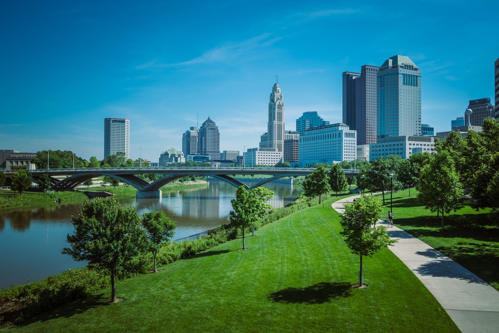 The Columbus skyline across the Scioto River with a park and bridge in the foreground