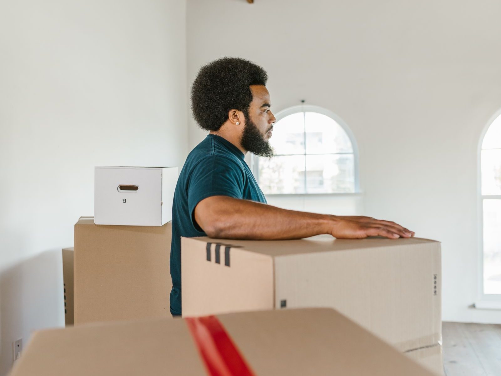 A mover in a dark t-shirt resting his hands on a taped cardboard box in an empty white room