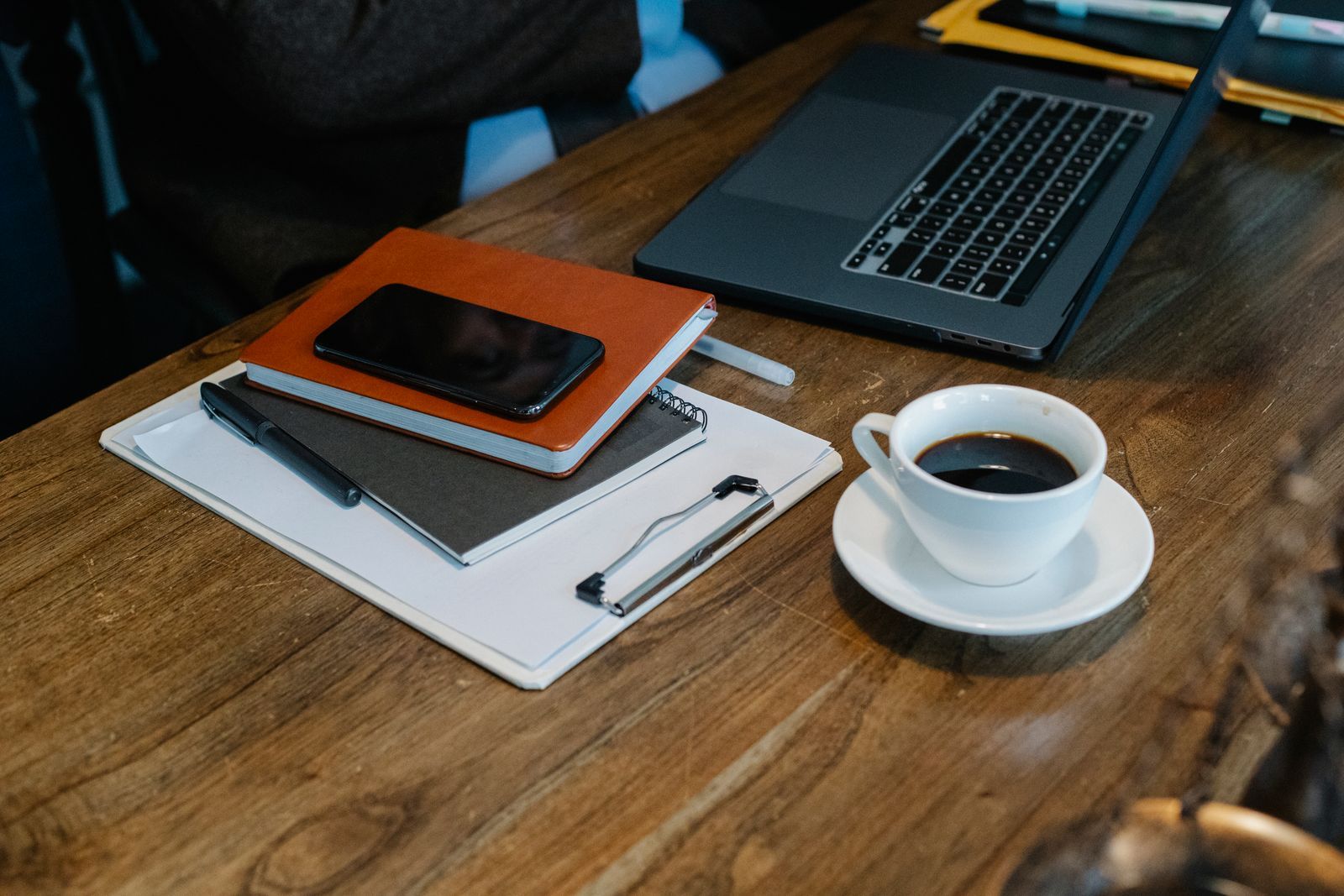 A phone resting on an open notebook beside a cup of coffee
