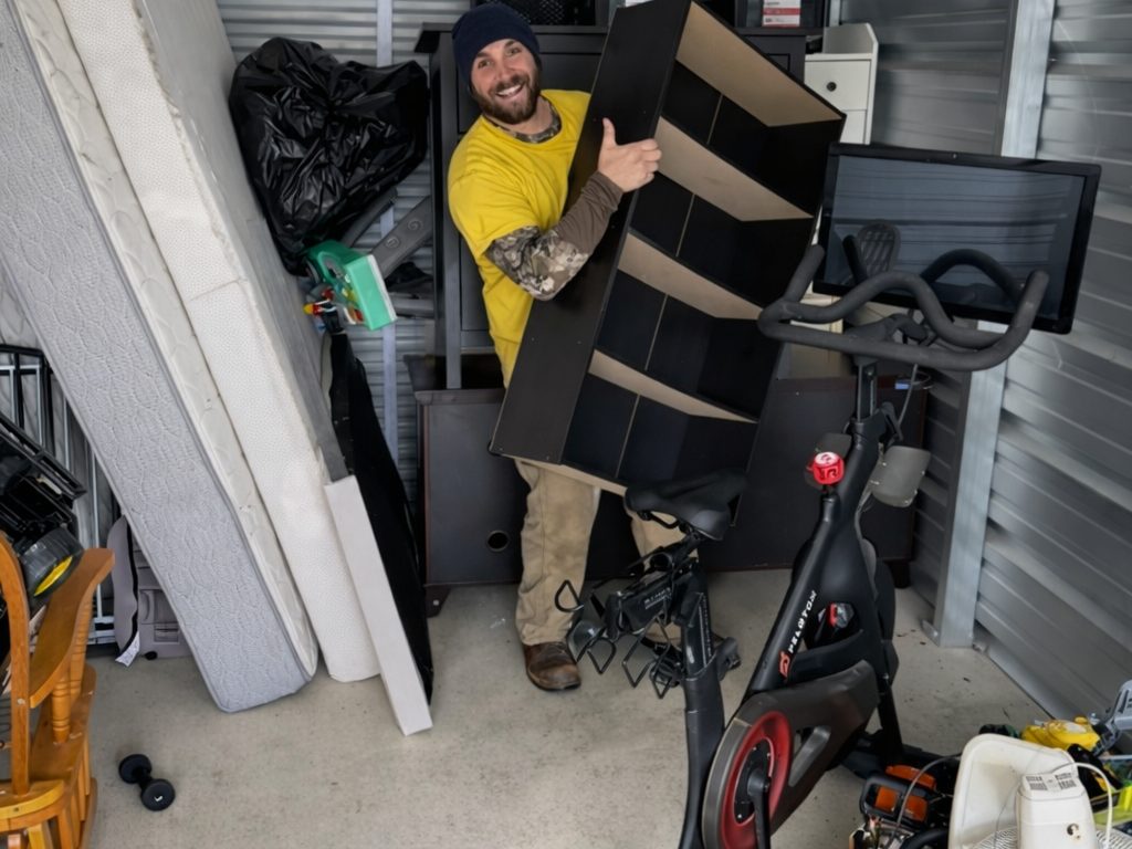 A Hercules mover carrying a bookshelf out of a storage unit full of furniture