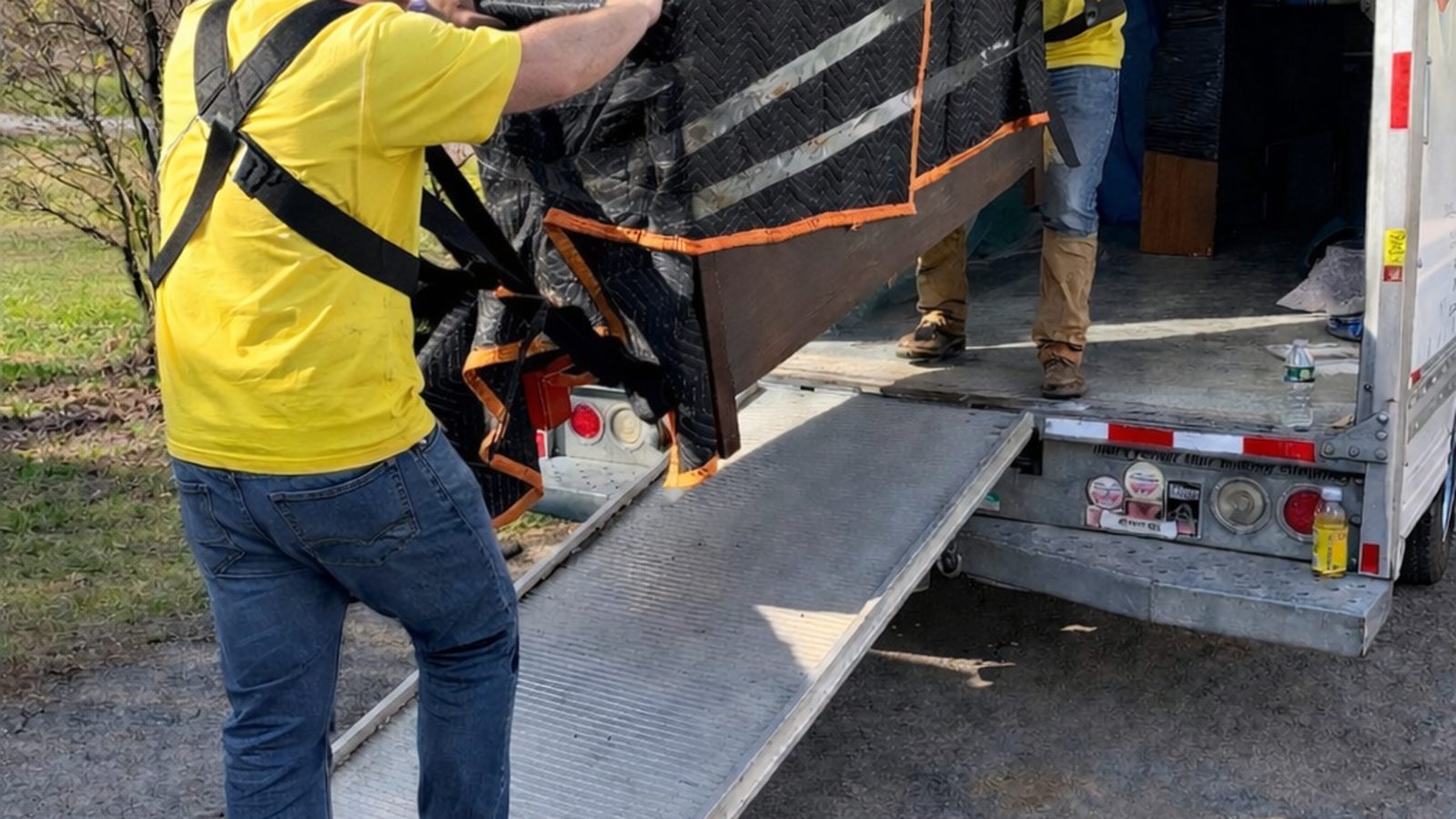 A dresser wrapped in stretch film and moving blankets sitting on the liftgate ramp of a truck