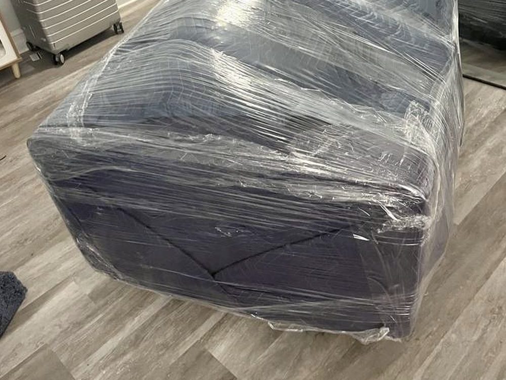 A sofa completely wrapped in clear stretch film sitting on a wood floor in an empty room