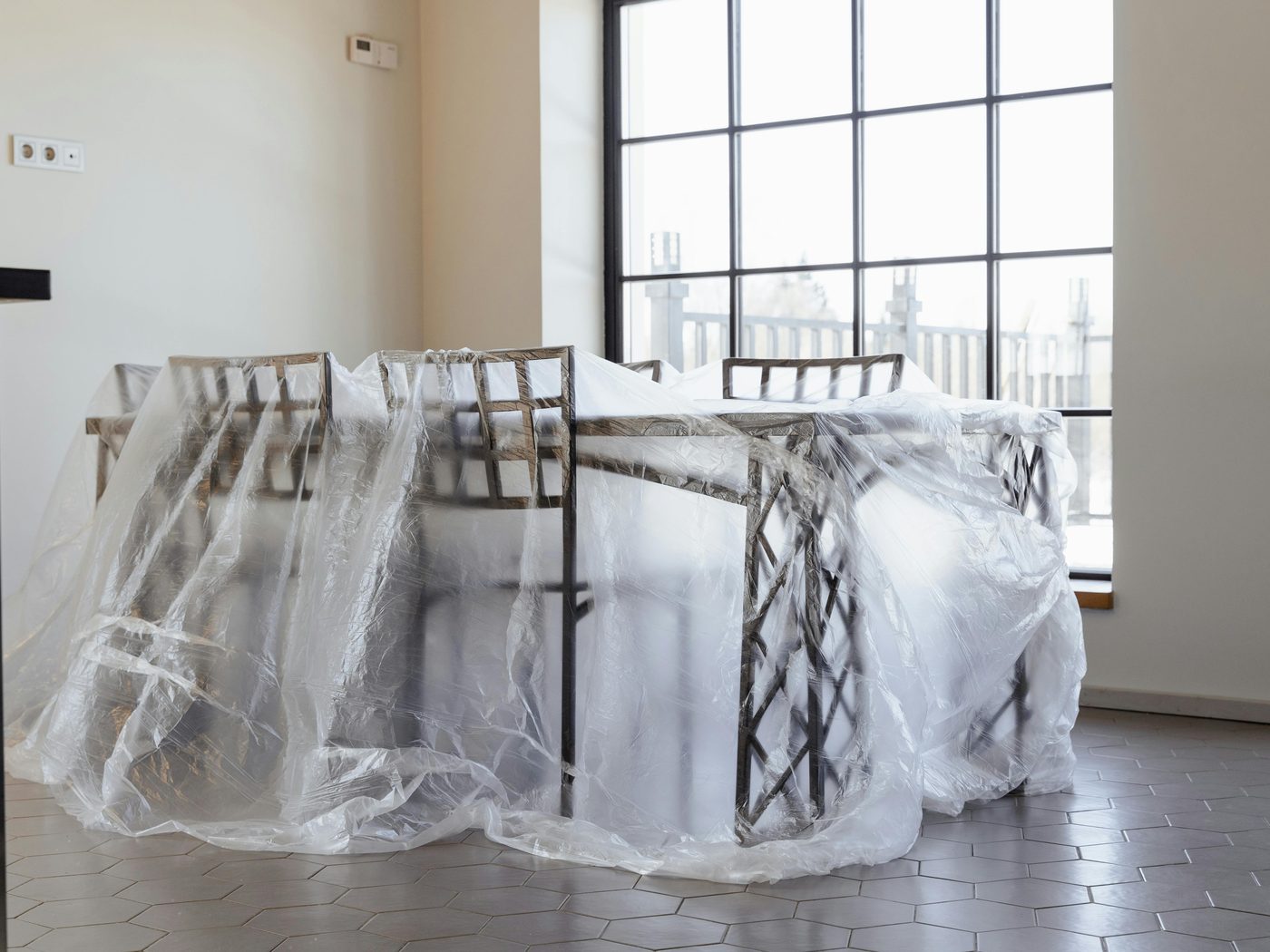 A glass dining table and chairs wrapped in stretch film in a sunlit empty room