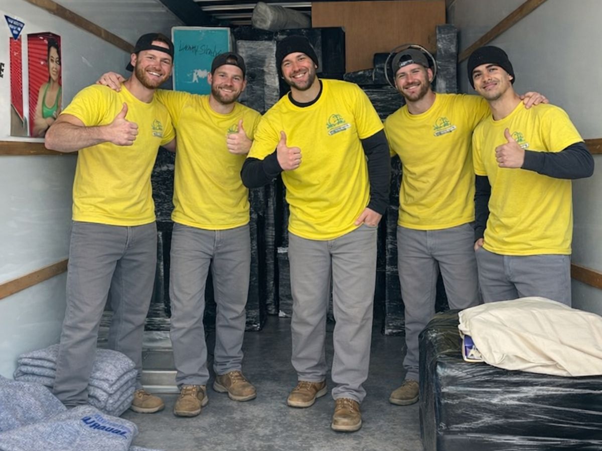 Five crew members in the back of a truck loaded with wrapped furniture