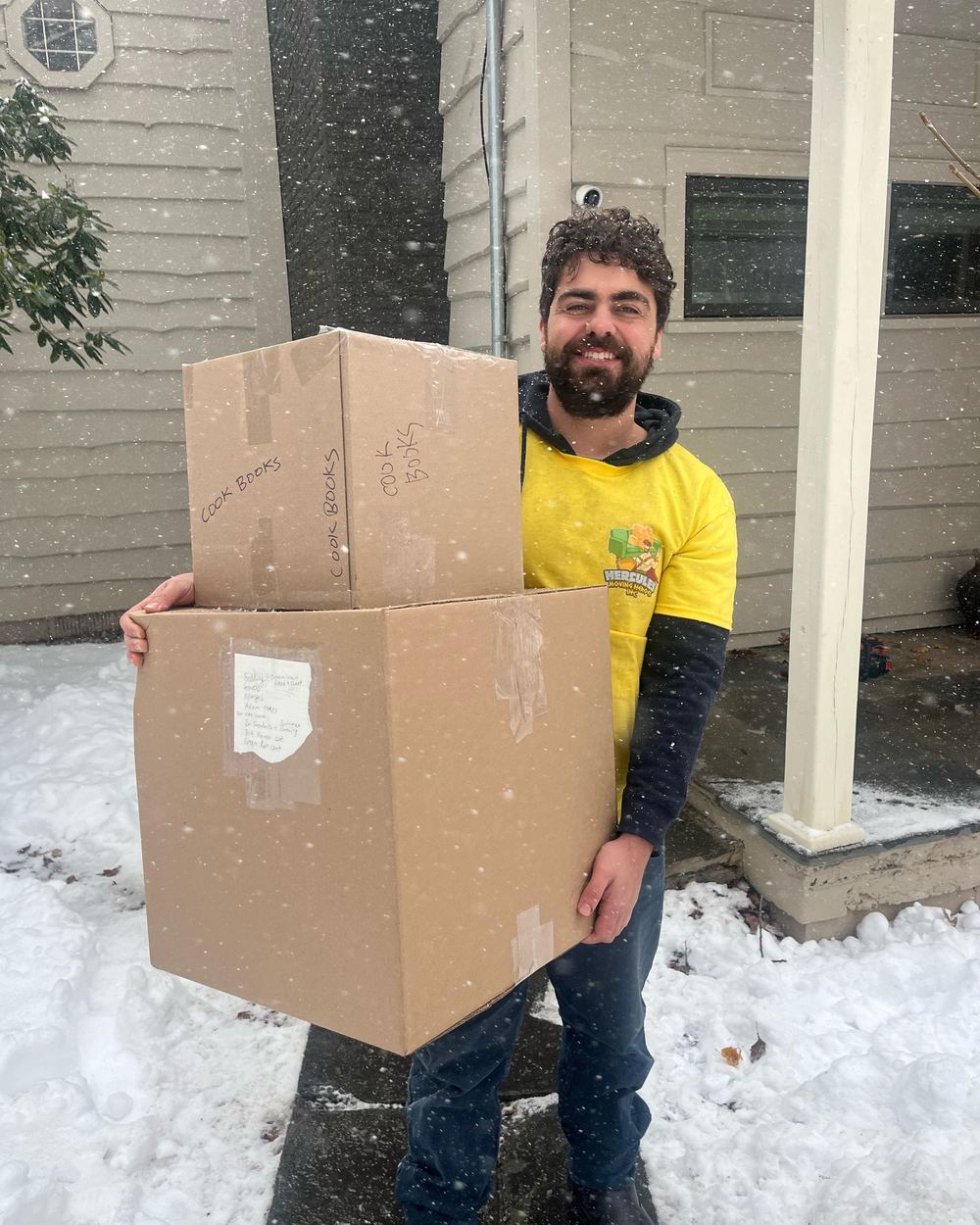 Jacob carrying two stacked cartons out of a house in falling snow
