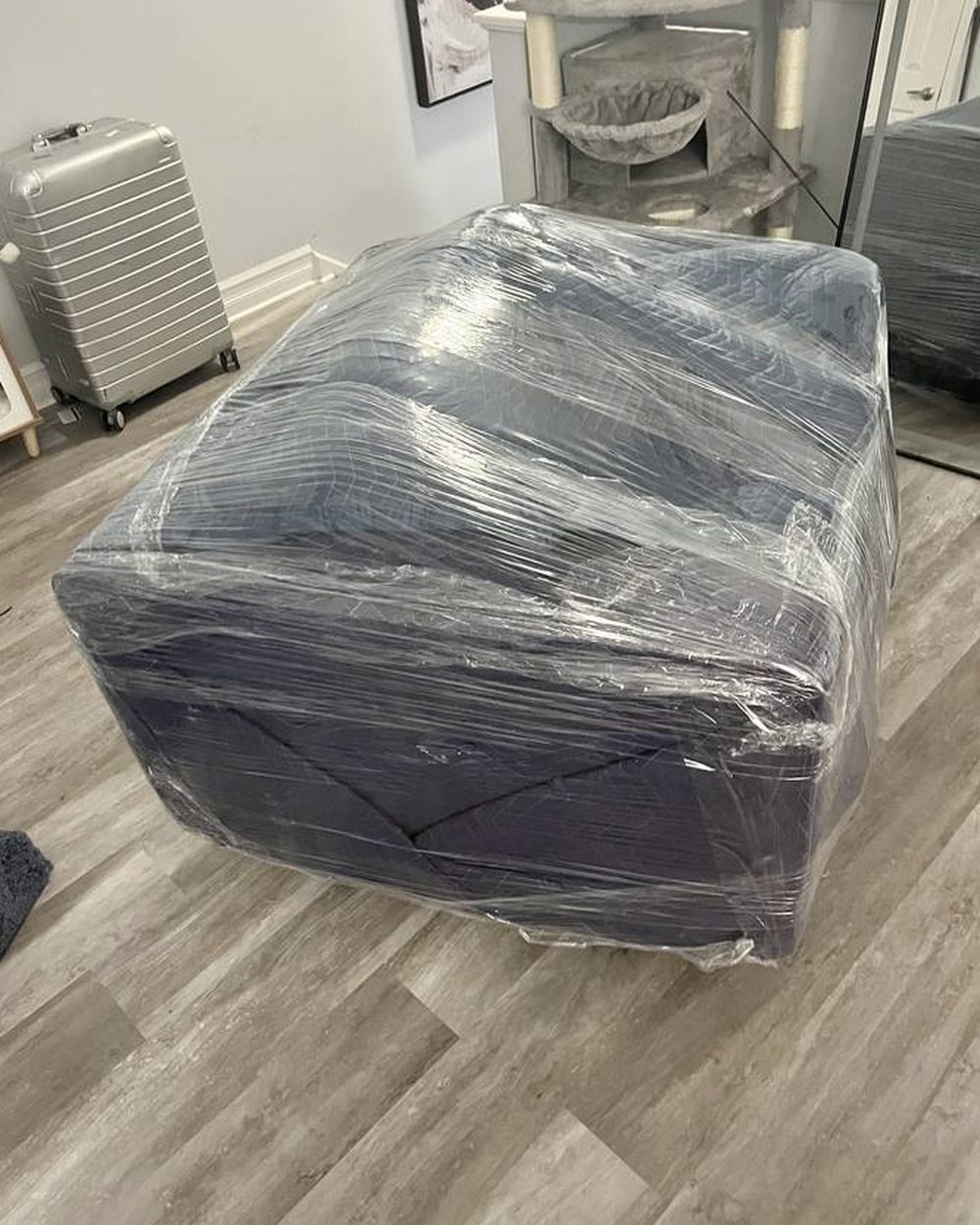 A dark sofa fully wrapped in stretch film sitting in an empty room with a hardwood floor